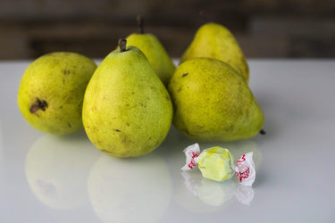 Taffy Town Golden Pear taffy candy in soft yellow-green resting beside fresh pears - gourmet salt water taffy with a delicate fruit flavor.